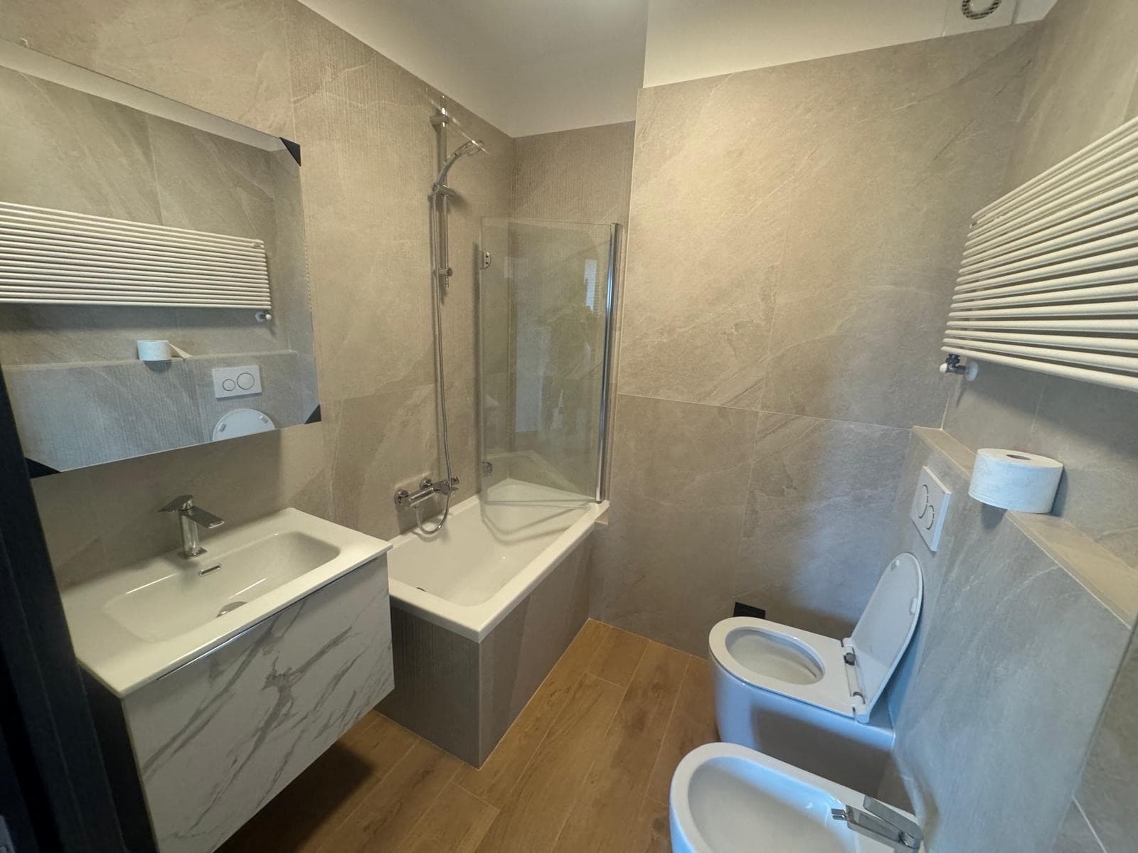 Bagno moderno con vasca, sanitari sospesi e rivestimenti effetto pietra