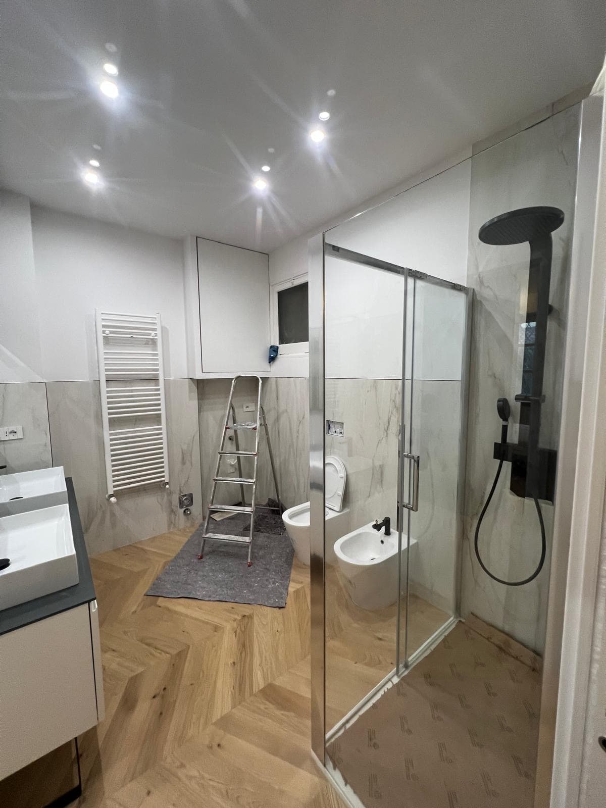 Bagno elegante con doccia in vetro e rivestimenti effetto marmo